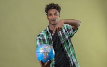 young african american traveler man holding globe pointing with finger to it looking at camera exited standing over green background young african american traveler man holding globe pointing with finger to it looking at camera exited standing over green background