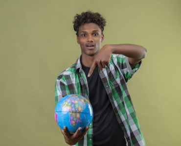 young african american traveler man holding globe pointing with finger to it looking at camera exited standing over green background young african american traveler man holding globe pointing with finger to it looking at camera exited standing over green background